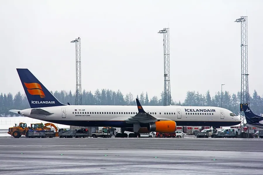冰島航空飛機停泊在濕滑機場停機坪,背景有地勤車輛和樹林。