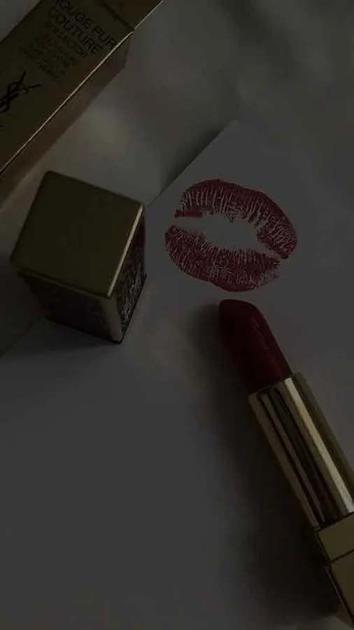 昏暗燈光下,金色外殼的奢華紅色唇膏和紙上大膽的唇印。