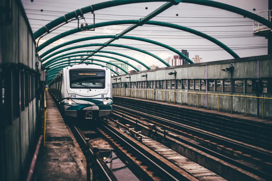 一列火車在都市環境中駛近綠色金屬天篷下的高架軌道。