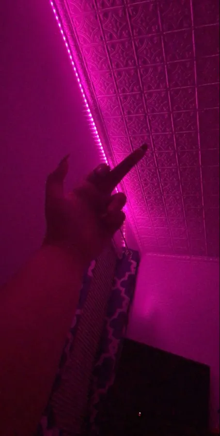 手指向有紋理天花板上的粉紅色LED燈帶照明。