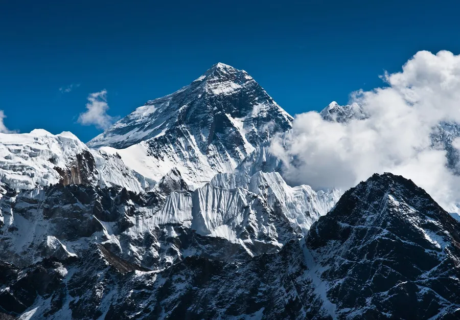 在清澈藍天下,白雪覆蓋的山峰聳立於雲層之上