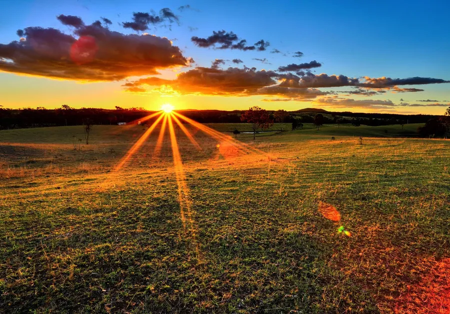 夕陽照耀草地,金色光芒與彩色雲朵。
