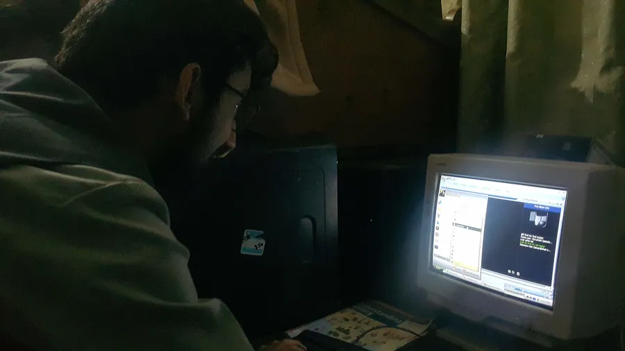 戴眼鏡的人在黑暗房間中使用舊電腦顯示器。