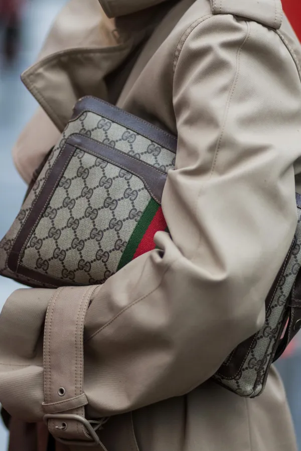 穿著米色乾濕褸的人拿著Gucci monogram肩袋。