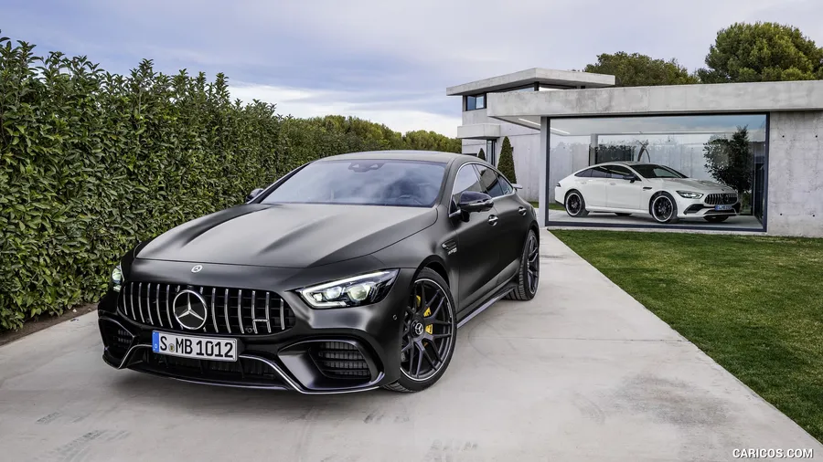 啞光黑色Mercedes-AMG GT停泊在現代玻璃車庫外,裡面有一輛白色AMG。