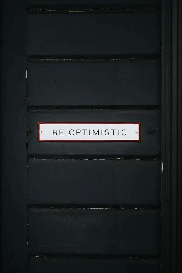 一扇黑色門,上面有一個白色標牌,寫著 be optimistic。