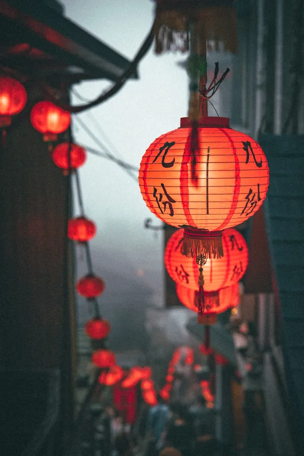 帶有黑色字符的紅色紙燈籠在黃昏時分霧氣瀰漫的小巷中溫暖地發光。