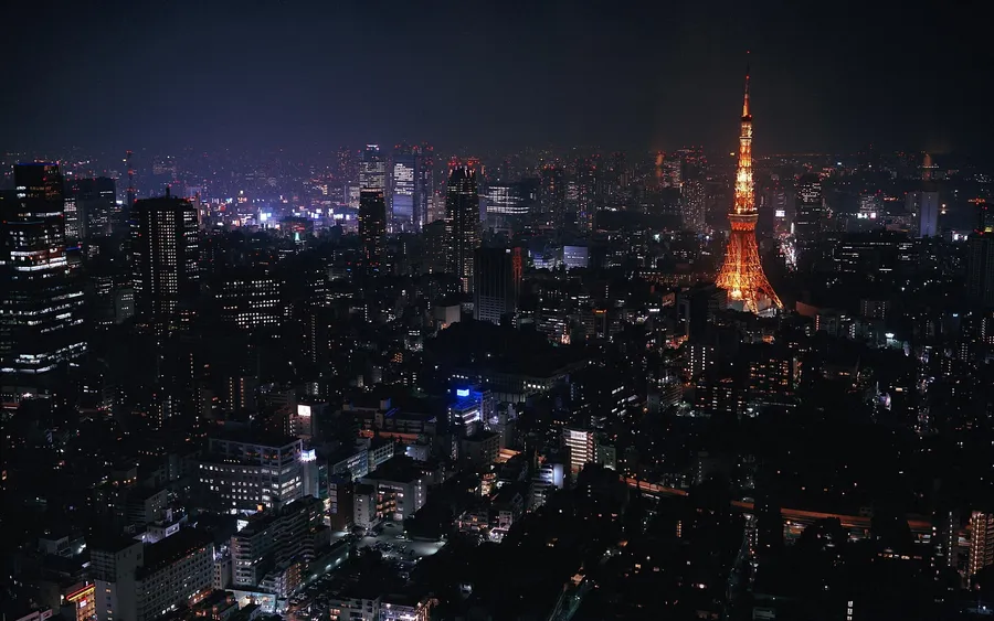 東京鐵塔在夜間亮起,映襯著黑暗的城市景觀。