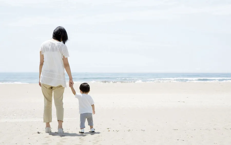 母親和幼兒手牽手在沙灘上走向海洋。