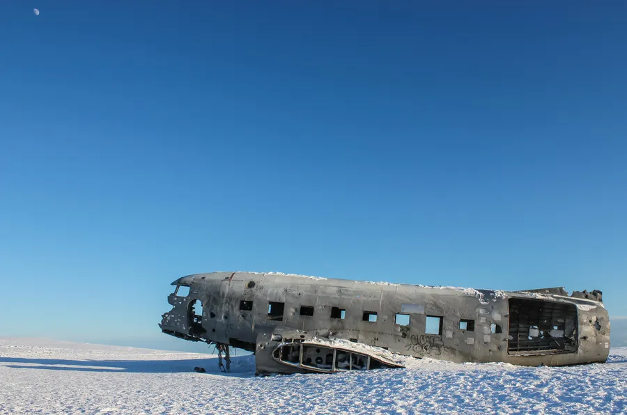 生鏽的飛機機身被遺棄在雪地上,天空清澈湛藍,可見月亮