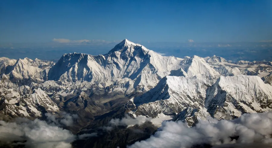 在清澈藍天下,雪山峰頂聳立於雲層之上。