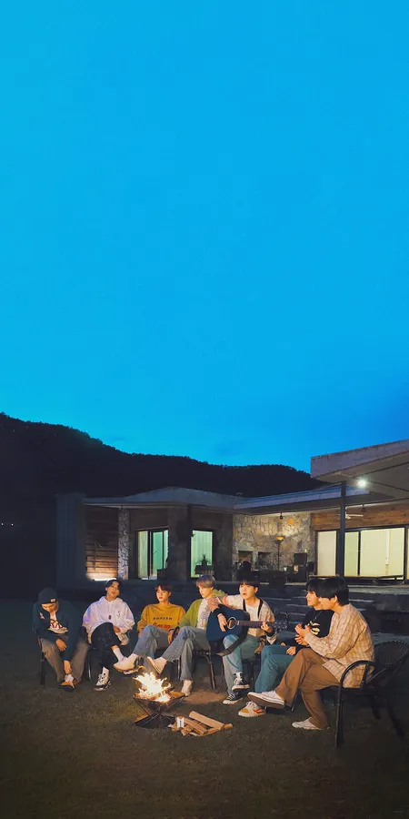 朋友們在黃昏時分坐在現代房屋前的營火周圍。