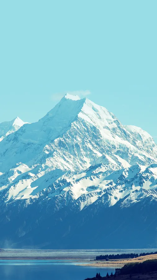 雪山峰俯瞰著晴朗天空下寧靜的藍色湖泊。