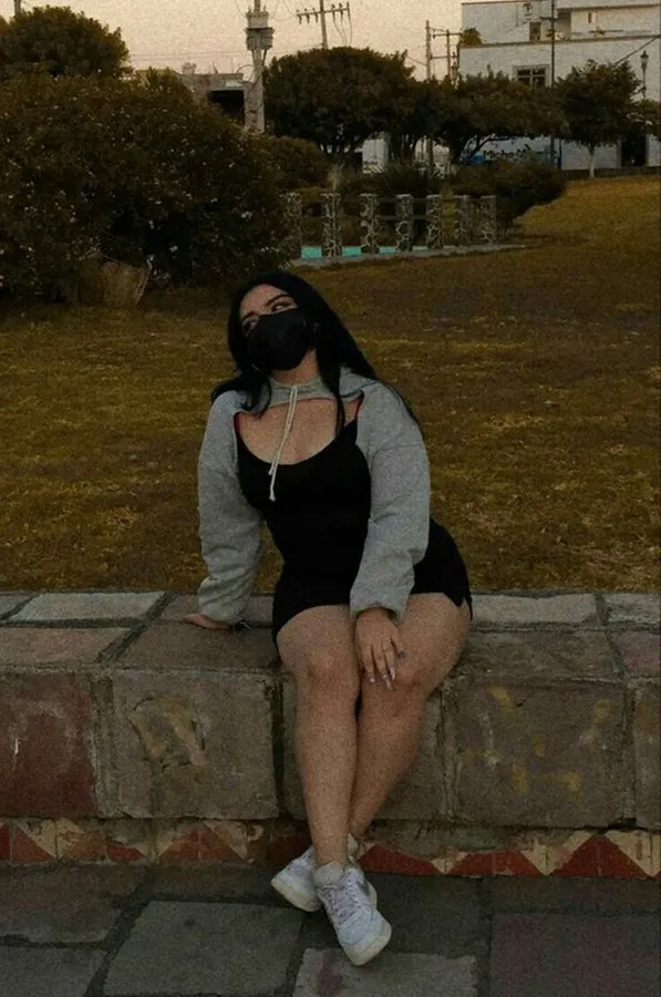 一個戴著口罩和連帽衫的人坐在公園的石牆上,在黃昏時分。