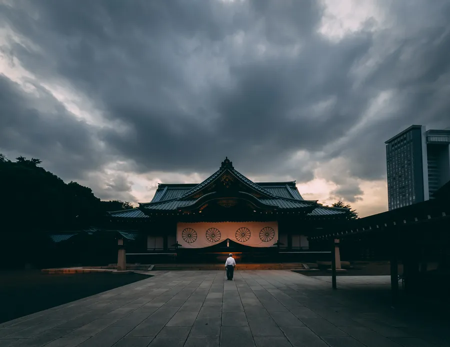 一個人在黑暗多雲的天空下走向傳統日本神社。