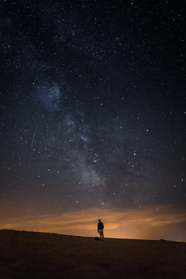 一個人在星空下站在沙漠沙丘上的剪影,銀河清晰可見。