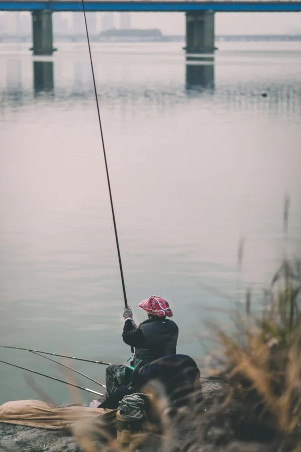喺河岸釣魚嘅人,背景有橋