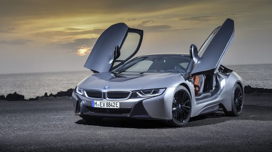 銀色BMW i8,鷗翼車門打開,停在日落時分的岩石海灘上。