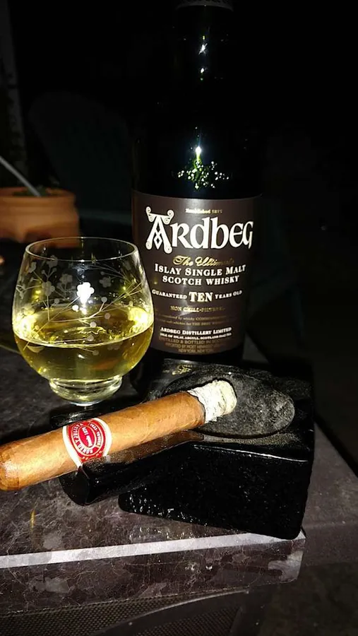 一瓶Ardbeg威士忌、一個杯子和一支雪茄在大理石表面上。