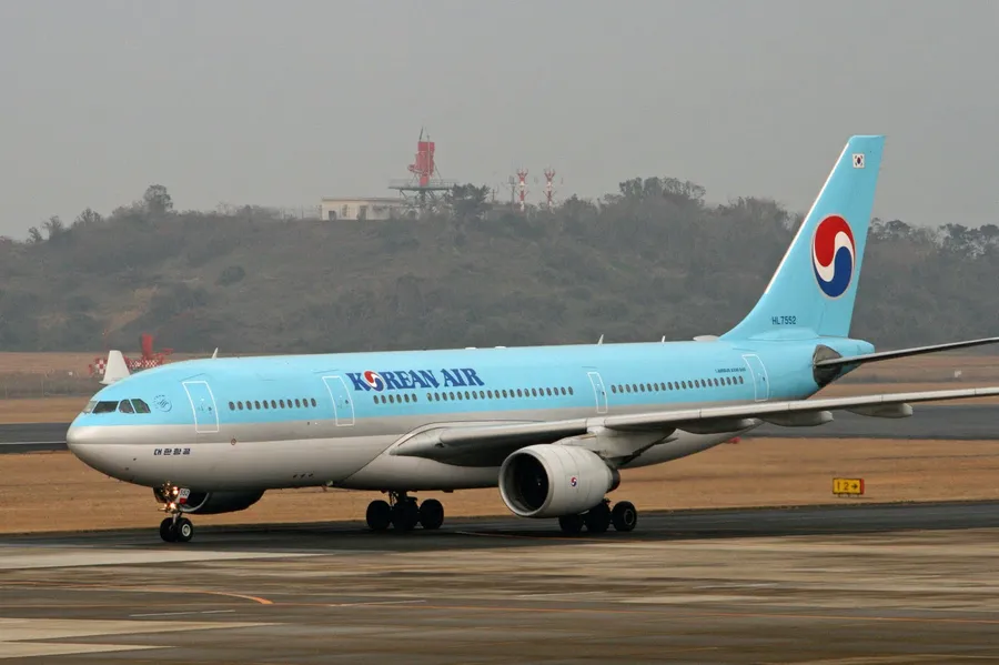 大韓航空飛機在機場跑道上,背景有朦朧山丘。