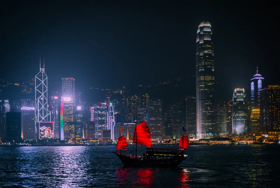 水上紅色帆船,背後是燈火通明的城市天際線