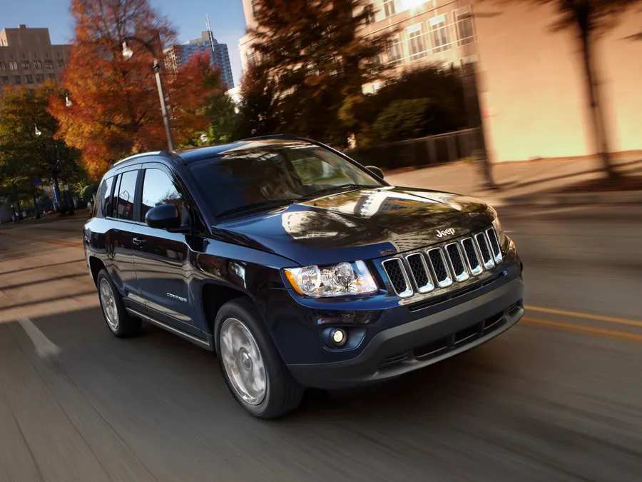 黑色Jeep Patriot在秋日城市街道上於日落時分行駛。