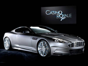 銀色Aston Martin DBS跑車在攝影棚中，背後有Casino Royale 75標誌屏幕。 — 汽車 壁紙