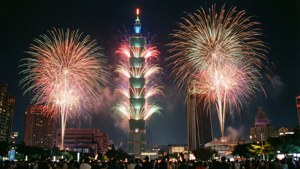 煙火照亮台北101大樓上方的夜空，下方有群眾觀看。