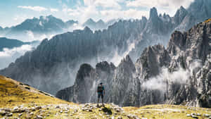 遠足者站在山脊上，面對下方有雲層的戲劇性岩石山峰。