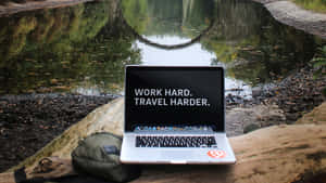 池塘旁圓木上的手提電腦，附有勵志語句 work hard travel harder