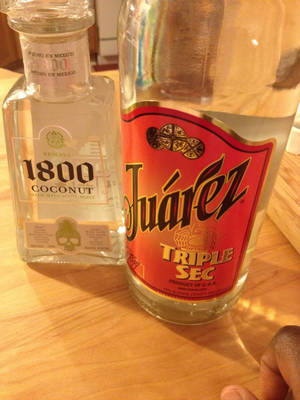 木桌上兩瓶酒，一隻手部分可見。
