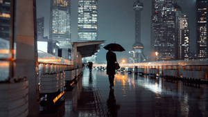 夜晚雨中城市人行道上撐傘行走的人，帶有倒影。