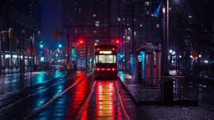 夜間城市中，在閃爍路燈和建築物下，潮濕軌道上的紅色電車。