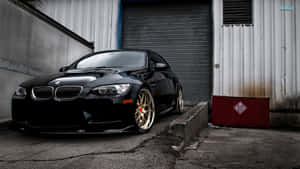 黑色BMW M3配金色輪圈，停在金屬車庫門前。