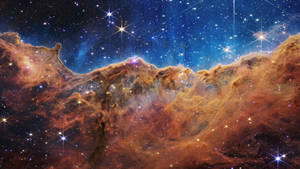 在深藍色太空中，發光的橙色星雲伴隨著閃爍的星星。 — 1920x1080 壁紙