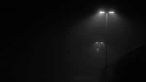 三盞街燈在夜間穿過濃霧發光，建築物輪廓在陰影中。