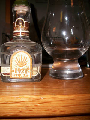 一瓶1921 Tequila Blanco和木吧台上的空玻璃杯。