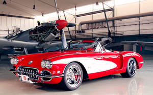 機庫內復古飛機旁邊的紅白經典Corvette開篷車。