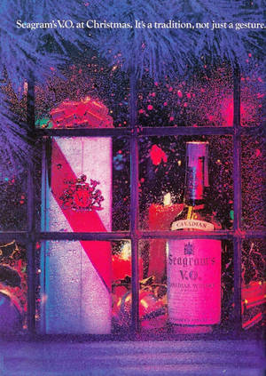 Seagram's V.O.威士忌酒瓶和禮品盒在節日櫥窗中展示，配有節日燈光。 — 雙螢幕桌布 壁紙