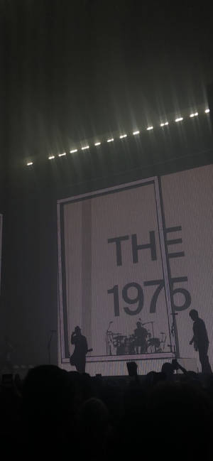 剪影音樂家在明亮的燈光下於舞台上表演，屏幕上顯示「THE 1975」。