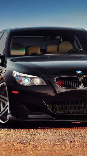 黑色BMW跑車，車頭燈閃爍，停在碎石路上。