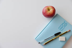 白色書桌上的紅蘋果和學校用品 — 激勵 壁紙