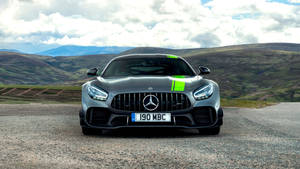 銀色 Mercedes-AMG GT 跑車在碎石路上，有山丘和雲朵。