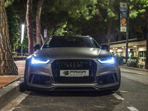 啞光灰色奧迪RS7，藍色車頭燈，夜間停放在松樹下。