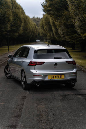 銀色福士 Golf GTI 停泊在潮濕的道路上，周圍有樹木。 — 哥爾夫球場 壁紙
