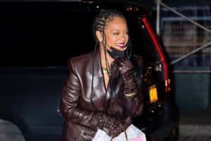 Rihanna 身穿棕色皮褸和飾釘手套，在夜晚的車旁微笑。