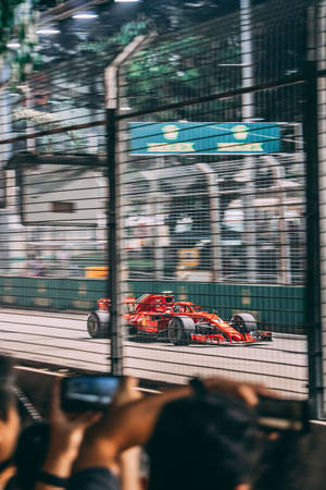 紅色F1賽車高速駛過圍欄，粉絲夜間拍攝。