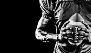 運動員在戲劇性燈光下以黑白方式持足球。 — NFL 美式足球 GIF 壁紙