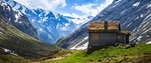 質樸木屋坐落在山谷中，周圍是白雪覆蓋的山峰和綠草。