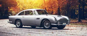 日落時分，秋日森林中的碎石路上停泊著銀色經典 Aston Martin DB5。